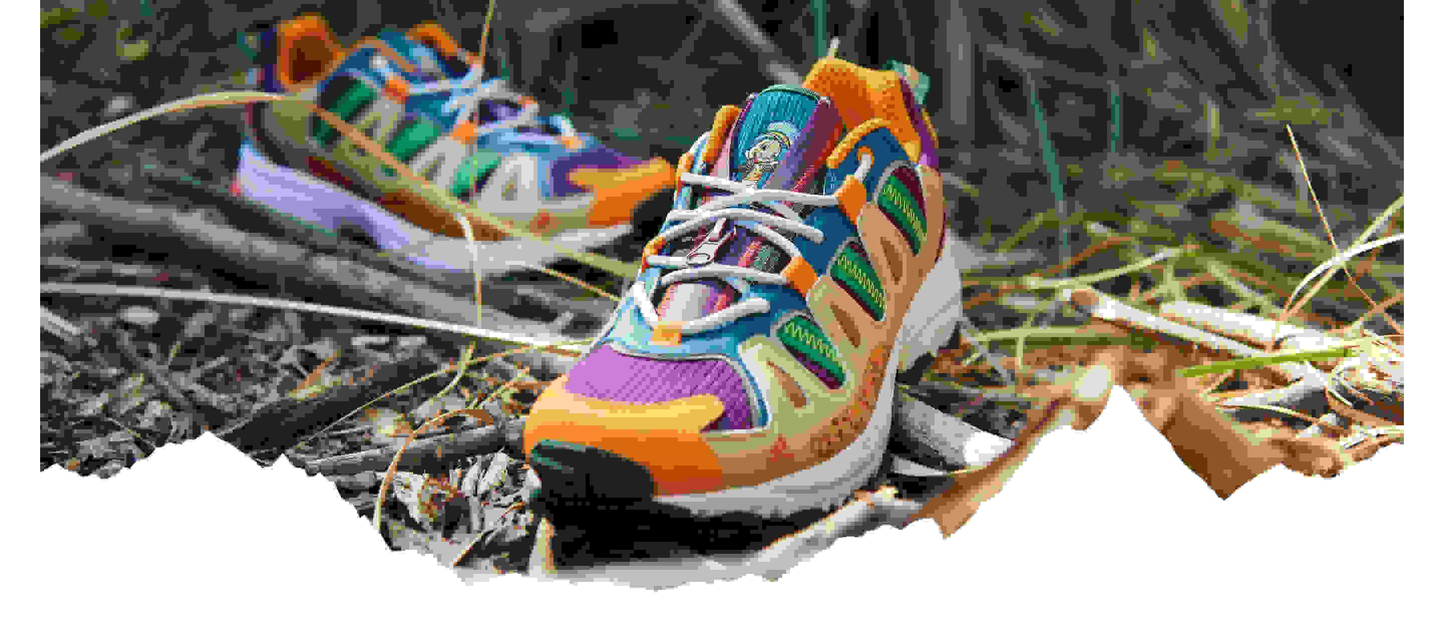 A pair of colourful Superturf Adventure sneakers on the ground, covered with sticks, branches and grass.