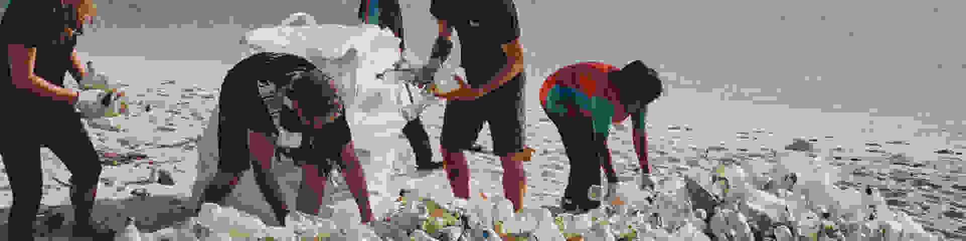 A group of people pickup up plastic waste on a beach under the hot sun