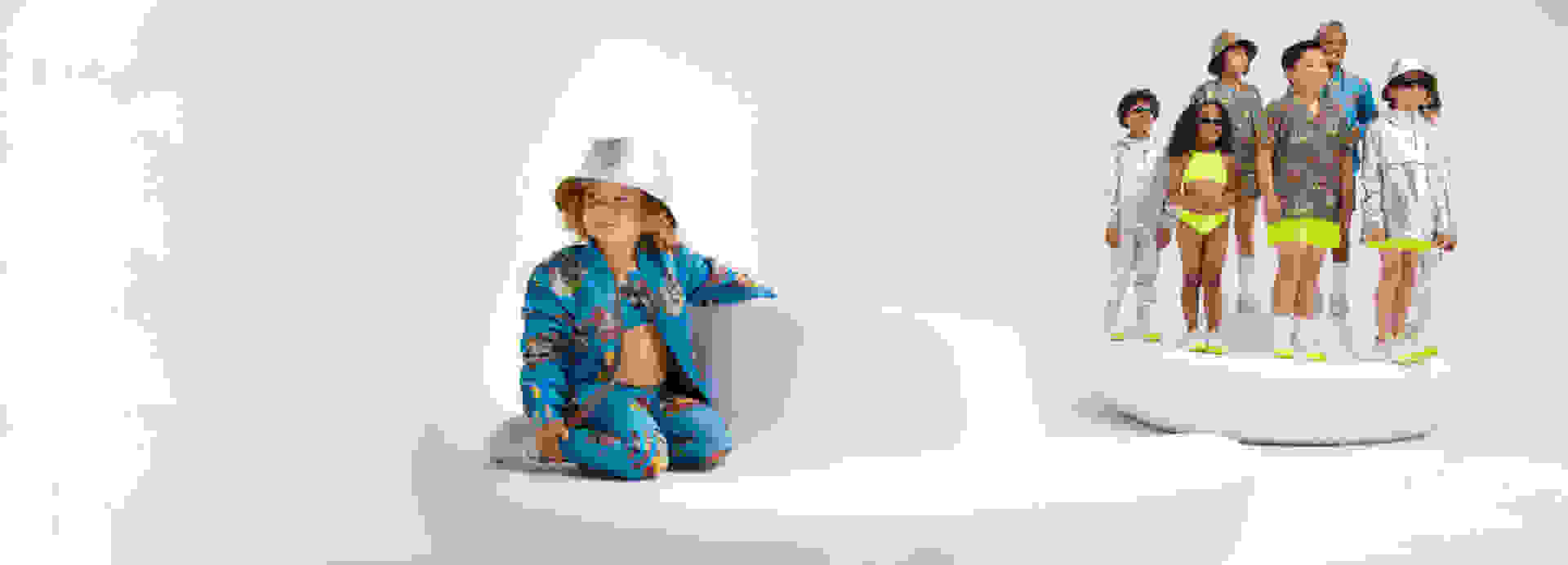 Kid wearing metallic hat and blue adidas x IVY PARK outfit sites on large seat while group of six kids stand smiling in the background.