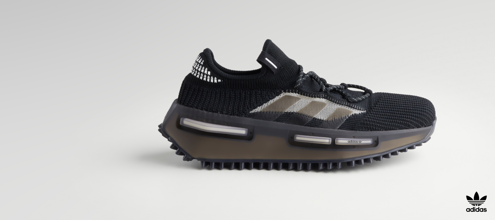 The black and grey NMD_S1 shoe pictured from the side on a white backdrop, showing off the boost cushioning and sleek textile upper.