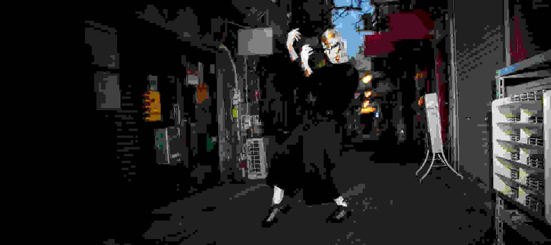 A person dances on a dark street while wearing black Y-3 apparel and a white and gold mask.