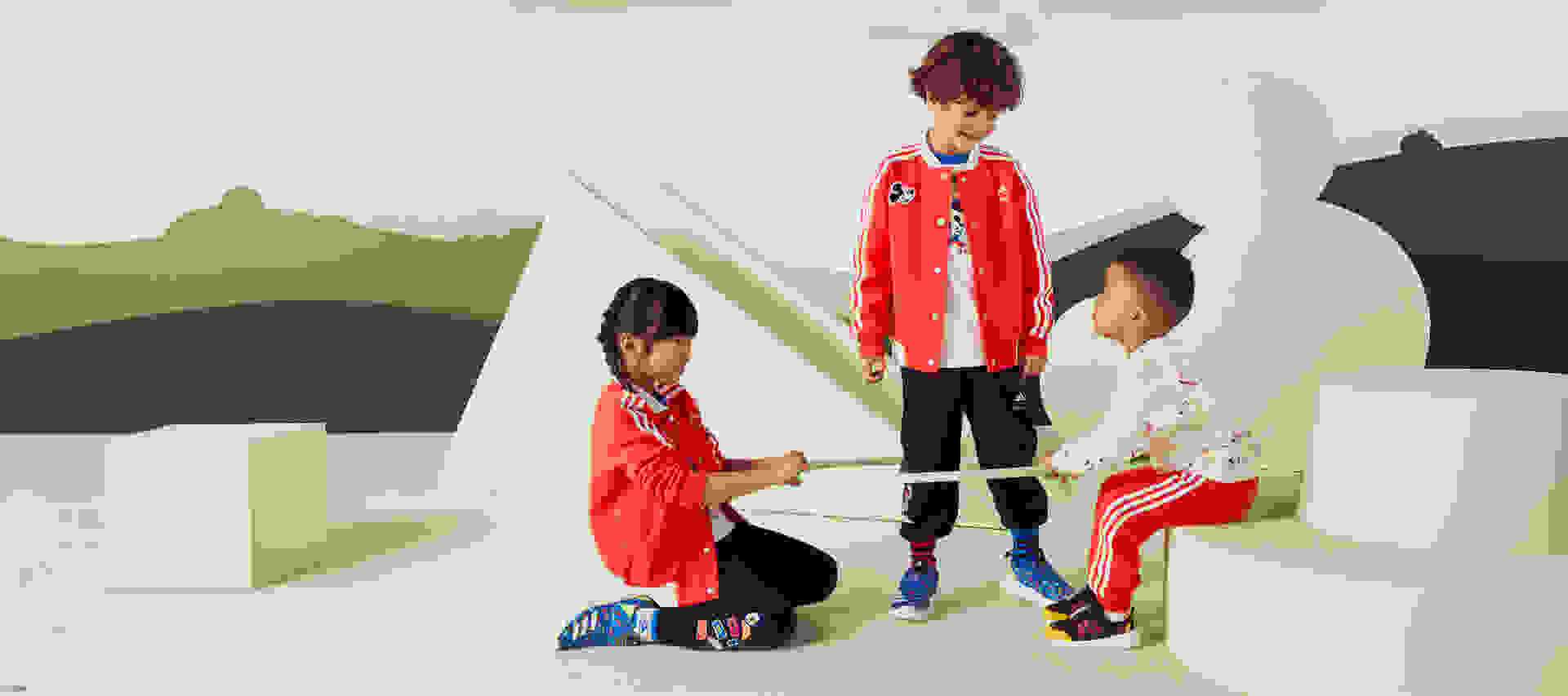 Two children holding a hula hoop while another child stands within it, all wearing the adidas | Mickey and Friends collection.