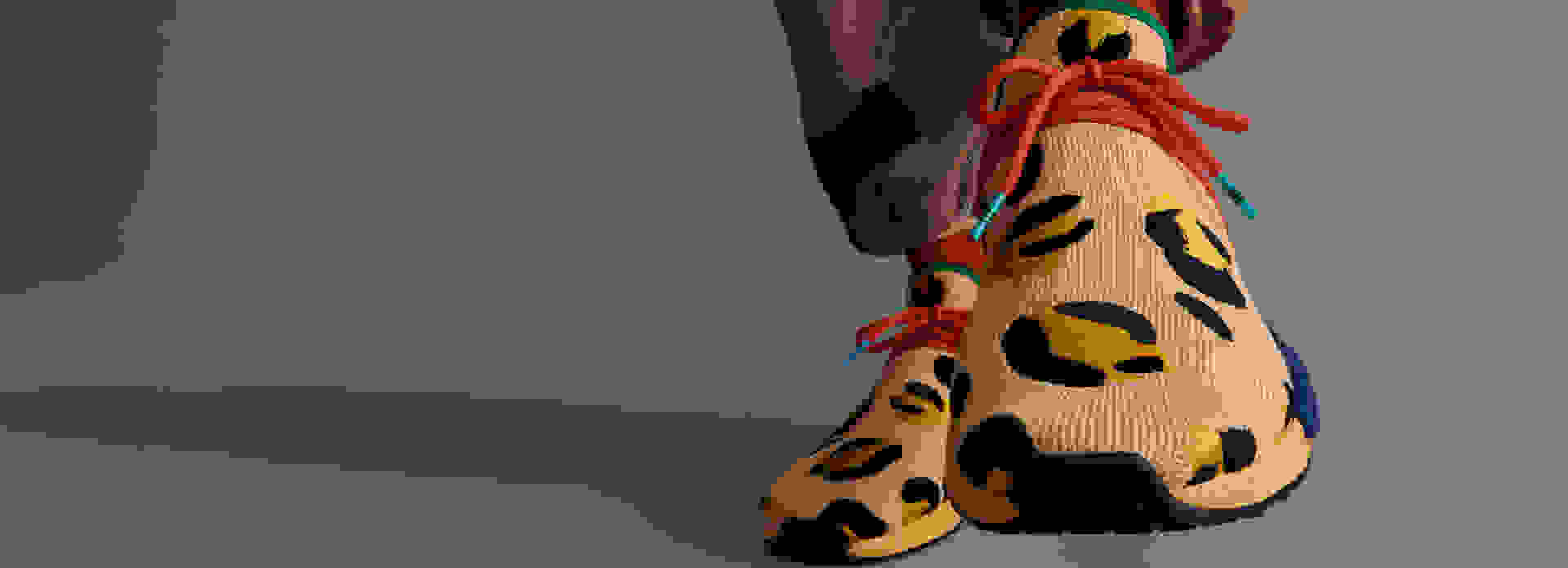 Front view of amber animal print shoe, as model wearing amber pants puts shoe on.