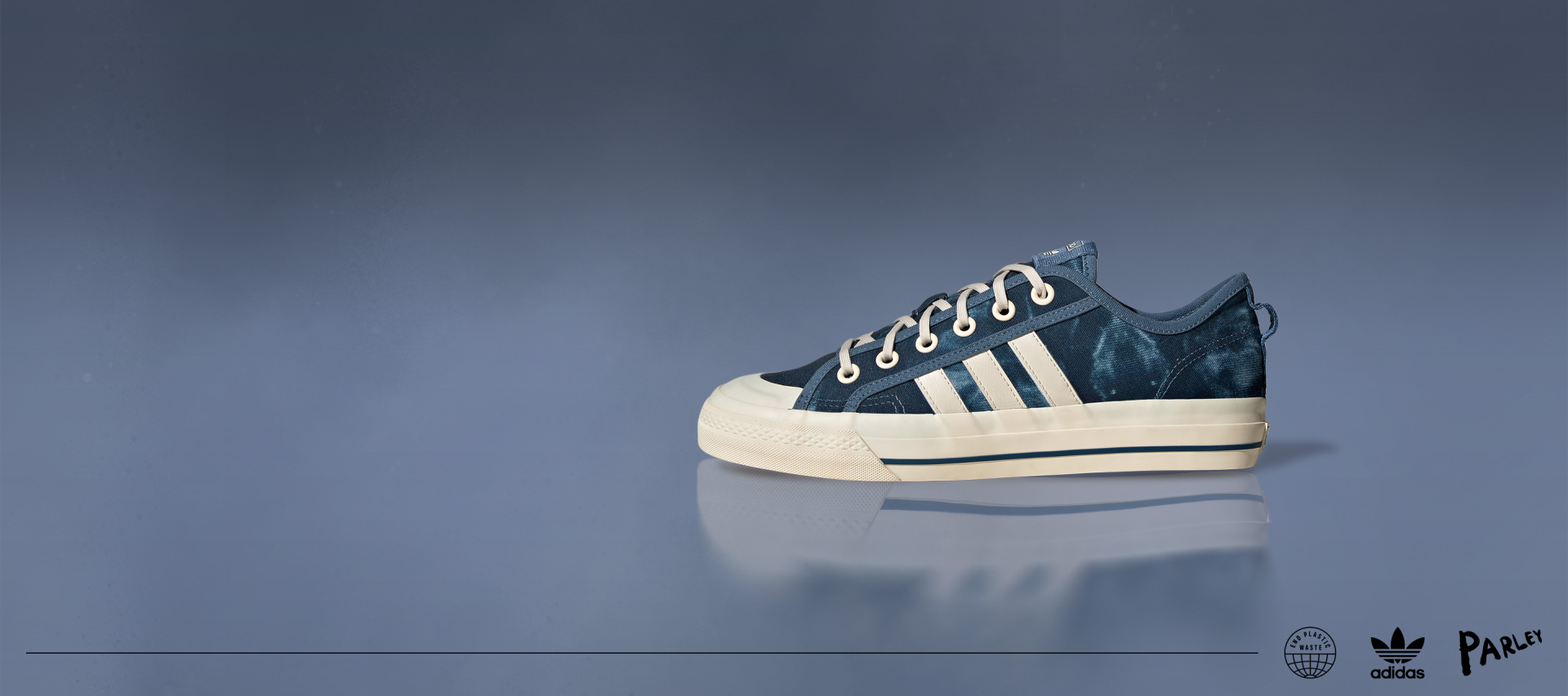 The dark blue, sun bleached Nizza sneaker is displayed from the side on a blue background, showing the white adidas 3-stripes.