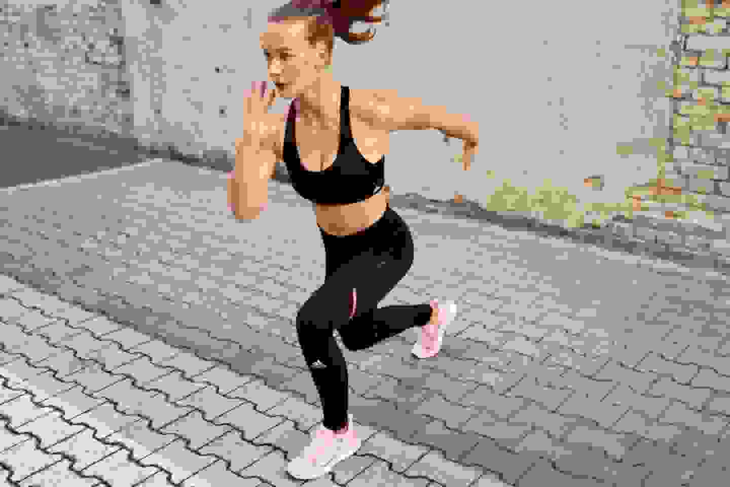 A woman wearing an adidas bra and tights holds a yoga pose in front of a concrete wall.