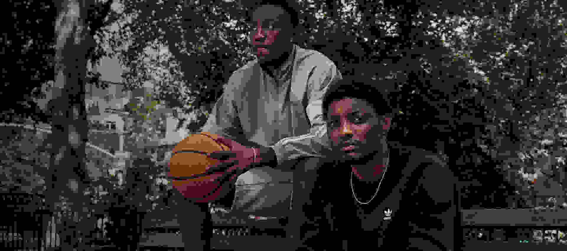 Two sitting men look to camera, one holding basketball
