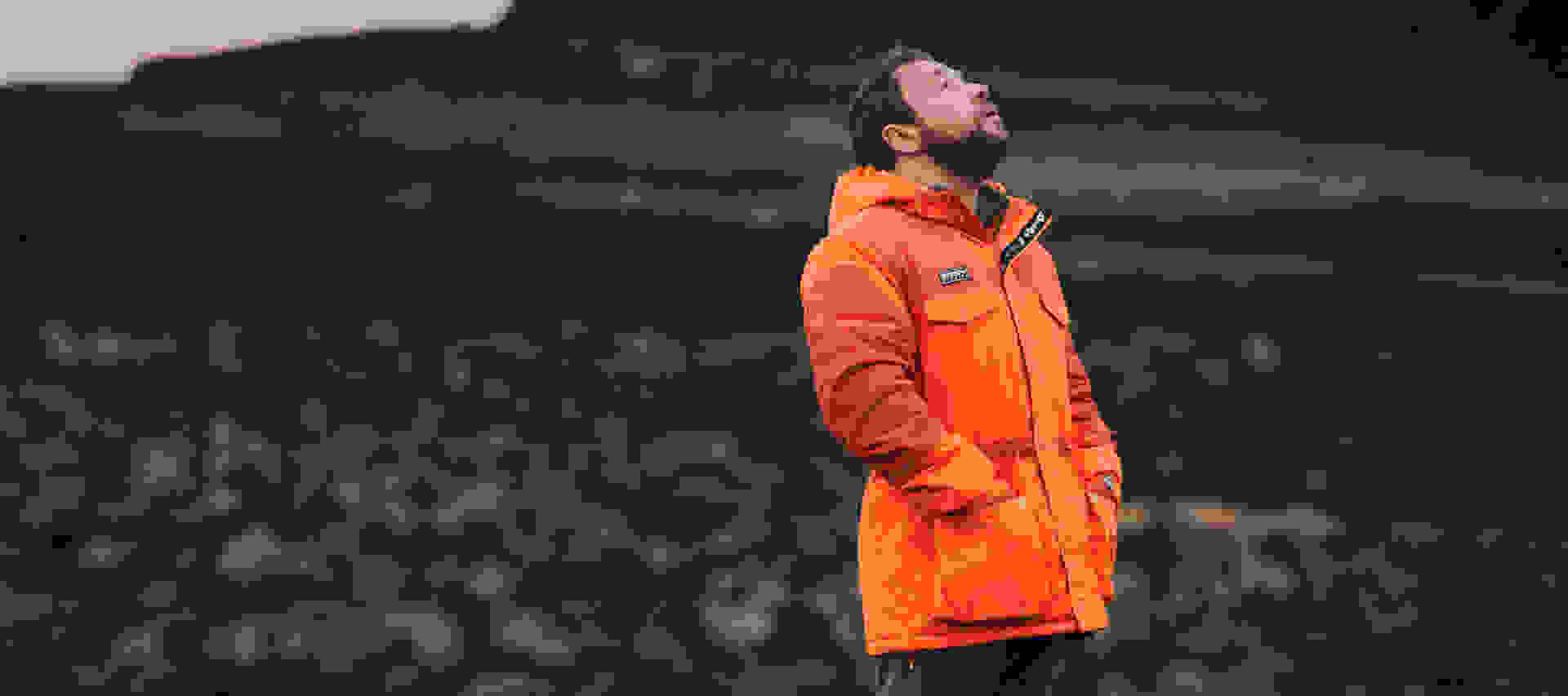 Stephen Graham stands in a stark Icelandic landscape, wearing an orange adidas Speizal jacket and gazing up at the sky.
