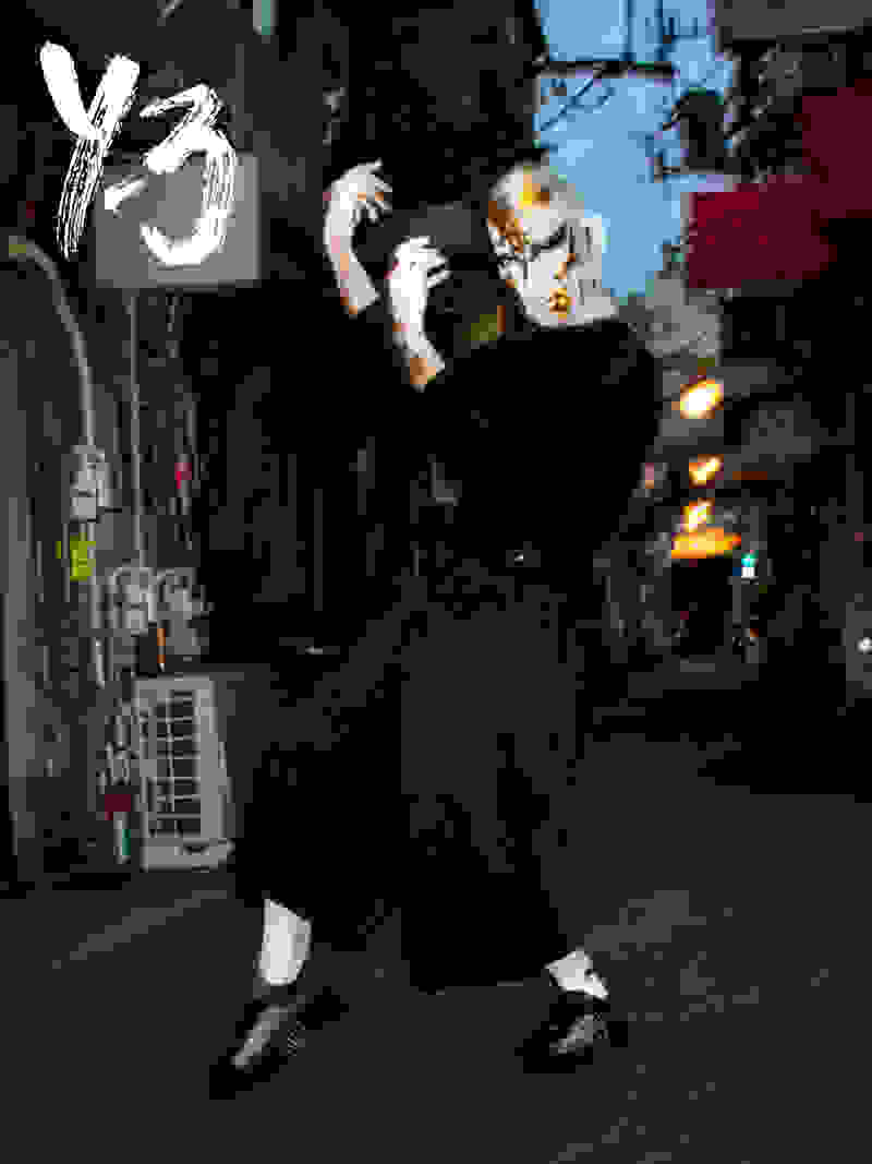 A person dances on a dark street while wearing black Y-3 apparel and a white and gold mask.