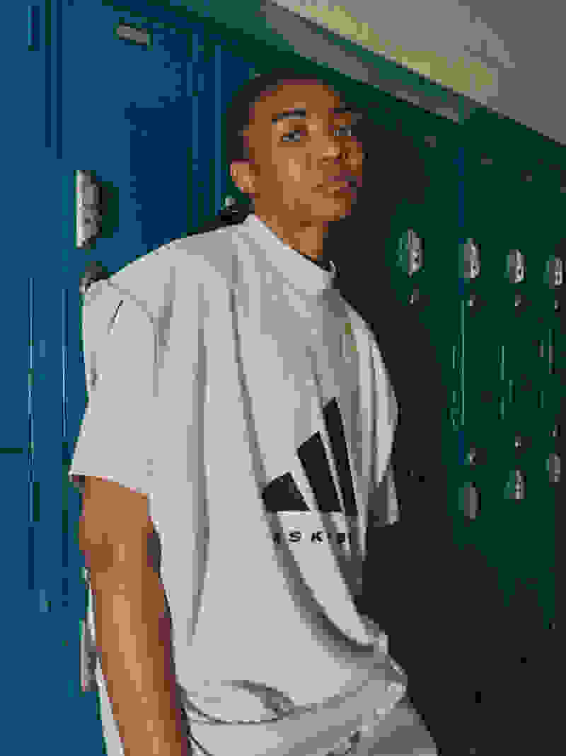 Model looks to camera, leaning against teal lockers
