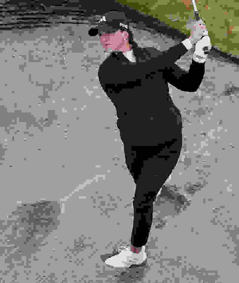 Women swinging a golf club in a bunker.