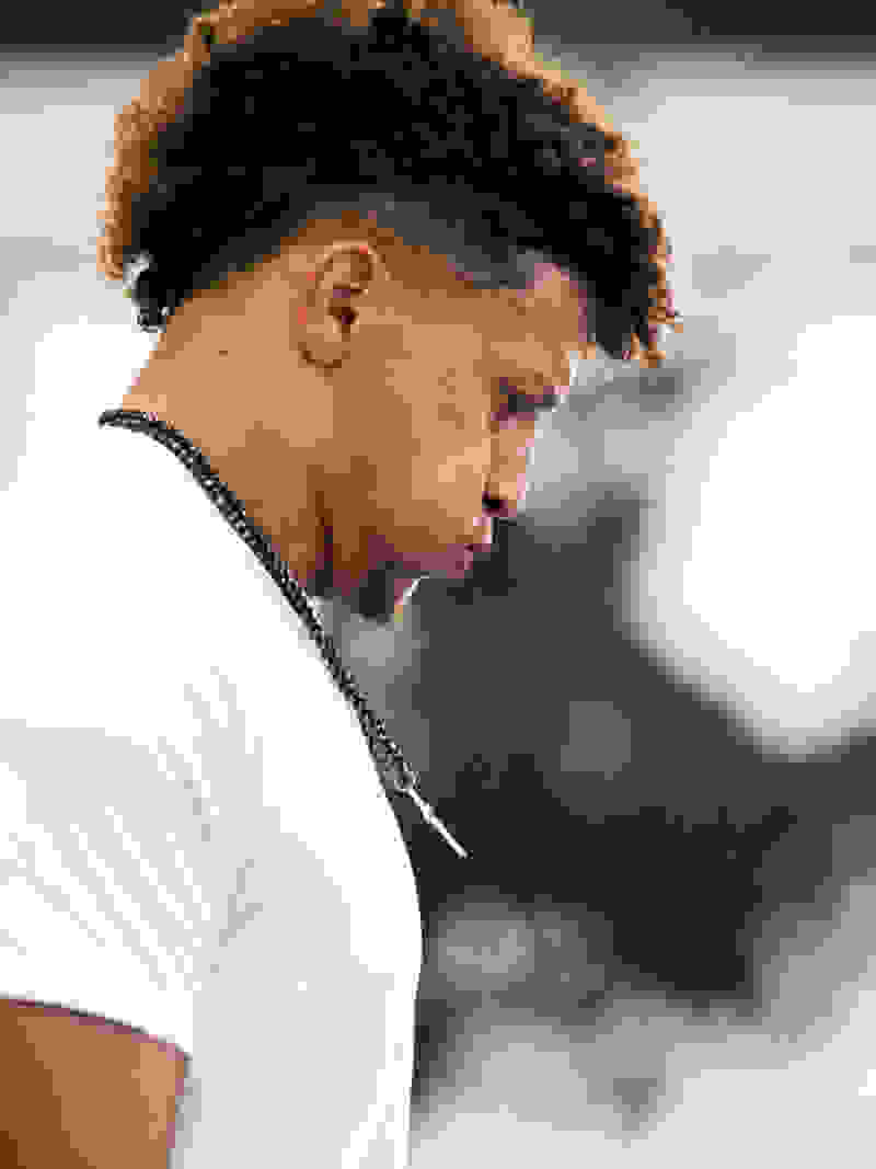 Patrick Mahomes is holding the football, looking out into the distance, about to launch ahead. He is wearing a white adidas T-shirt.