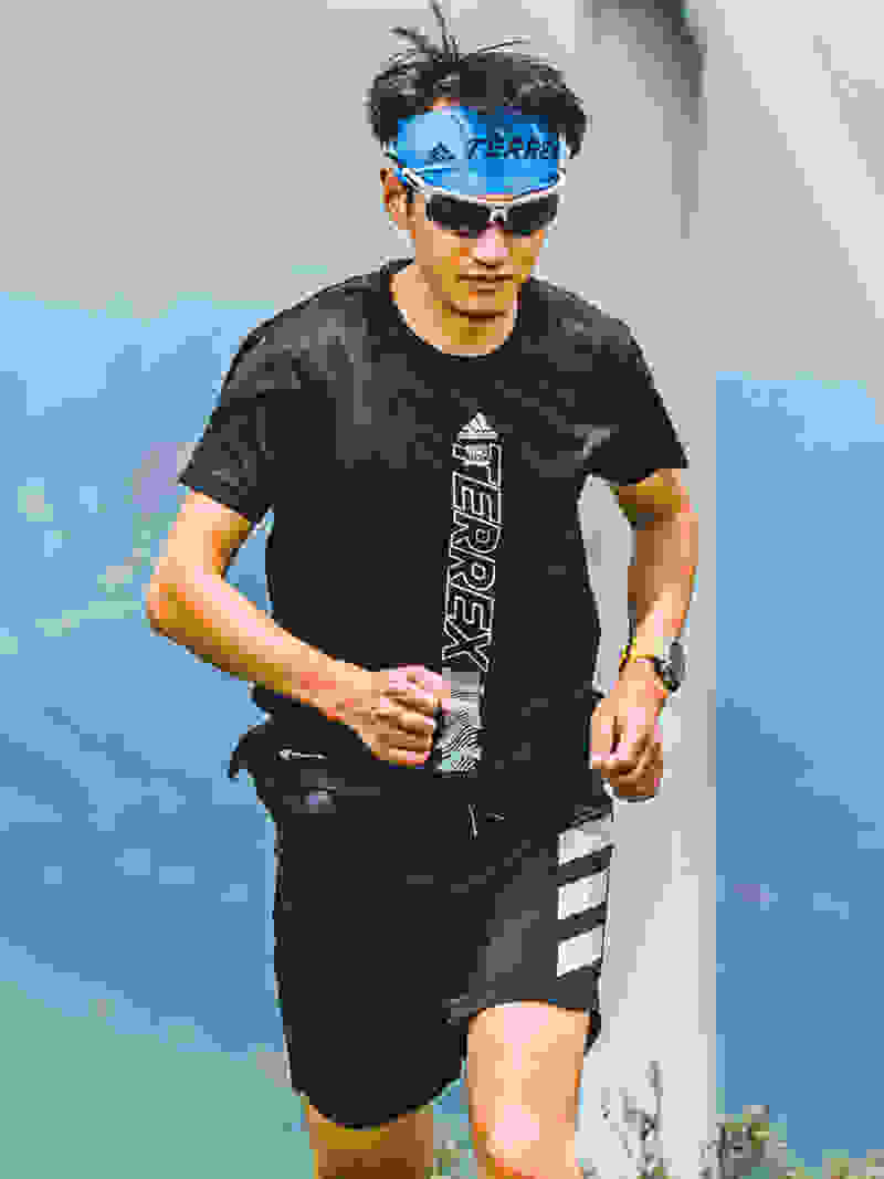 Male trail runner in black t-shirt and blue sweat band runs up a hill