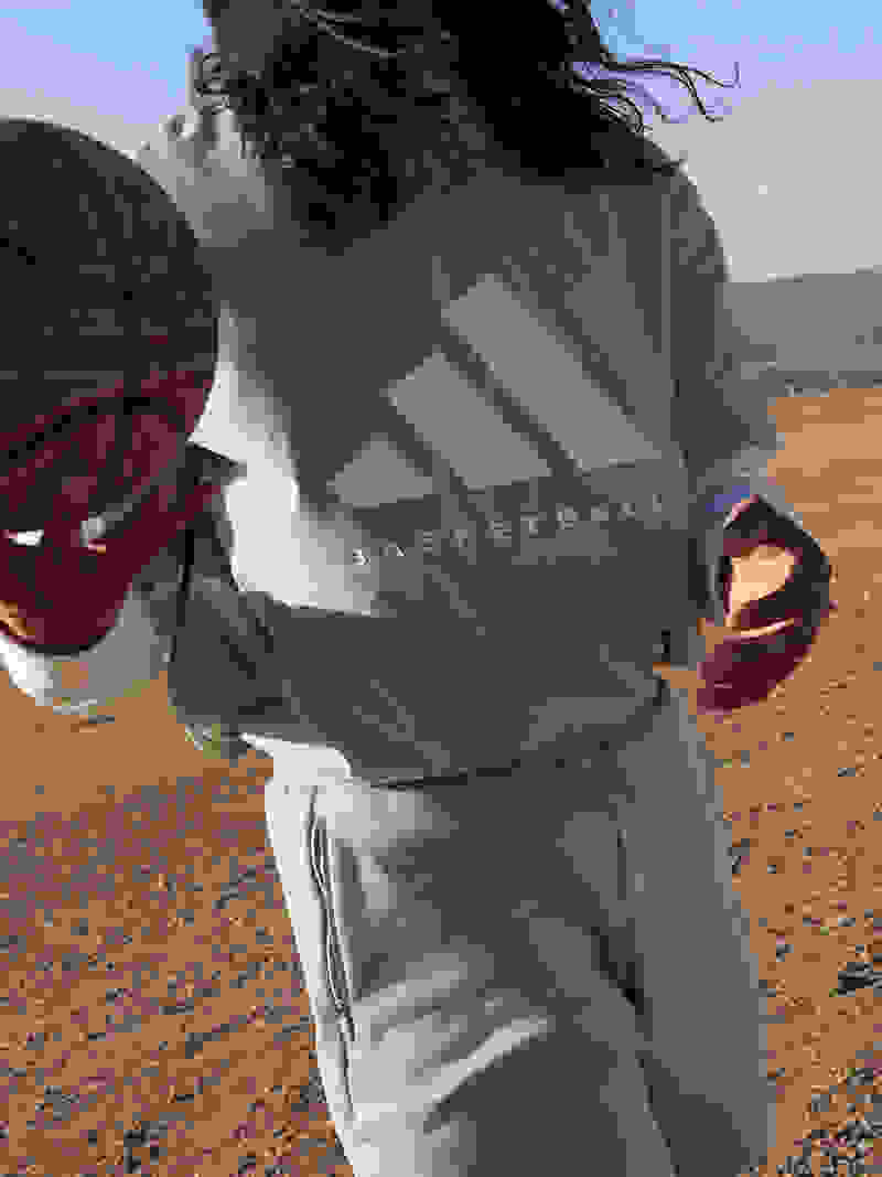 A person holding a basketball in their right hand, wearing a gray adidas Basketball shirt and shorts, standing in the desert with mountains and blue sky in the distance.