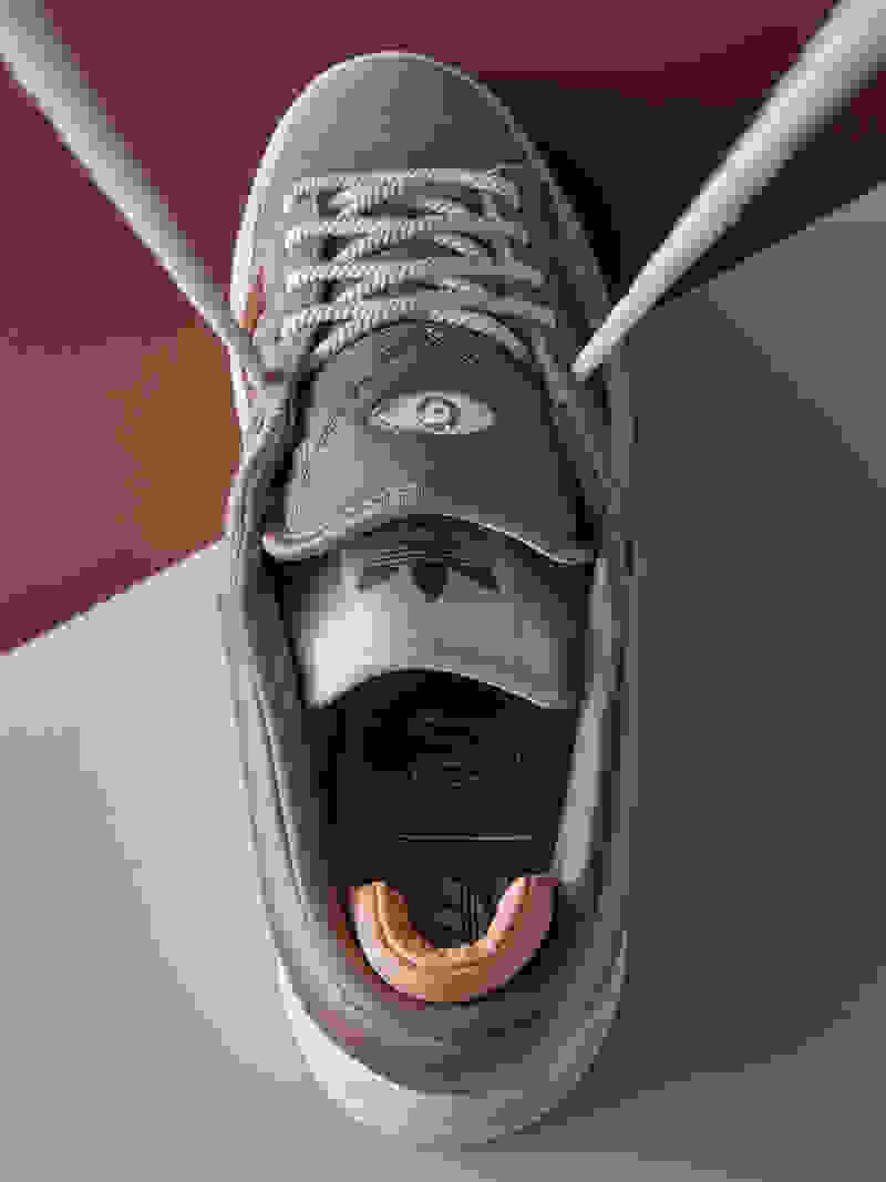 A pair of Bad Bunny Campus Chalky Brown sneakers are displayed on a two tone background.