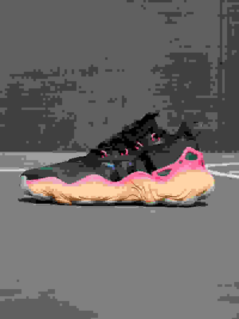 Side view of dark shoe with pink and orange sole on gray court floor.