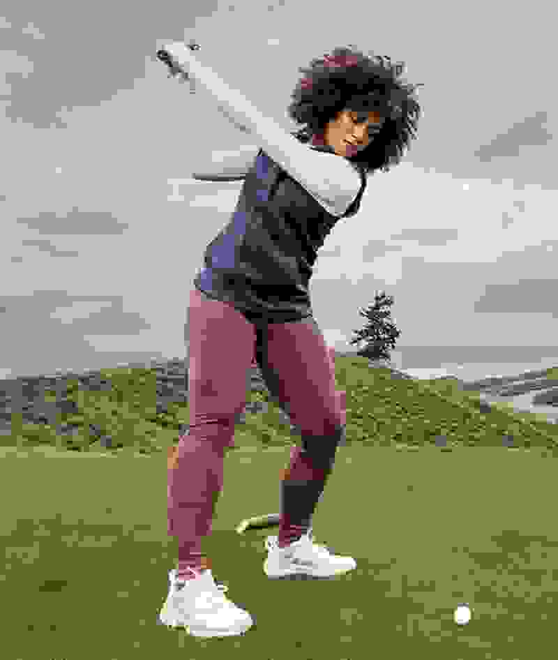 Woman in adidas fleece golf apparel swings a golf club.