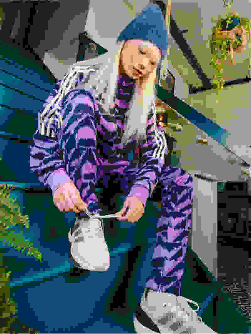Young woman dressed in purple adidas tracksuit sits on set of stairs tying up sneaker.