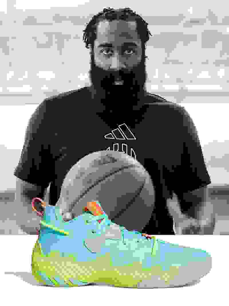 Professional basketball player James Harden holding a basketball with a multicolored shoe in the front.