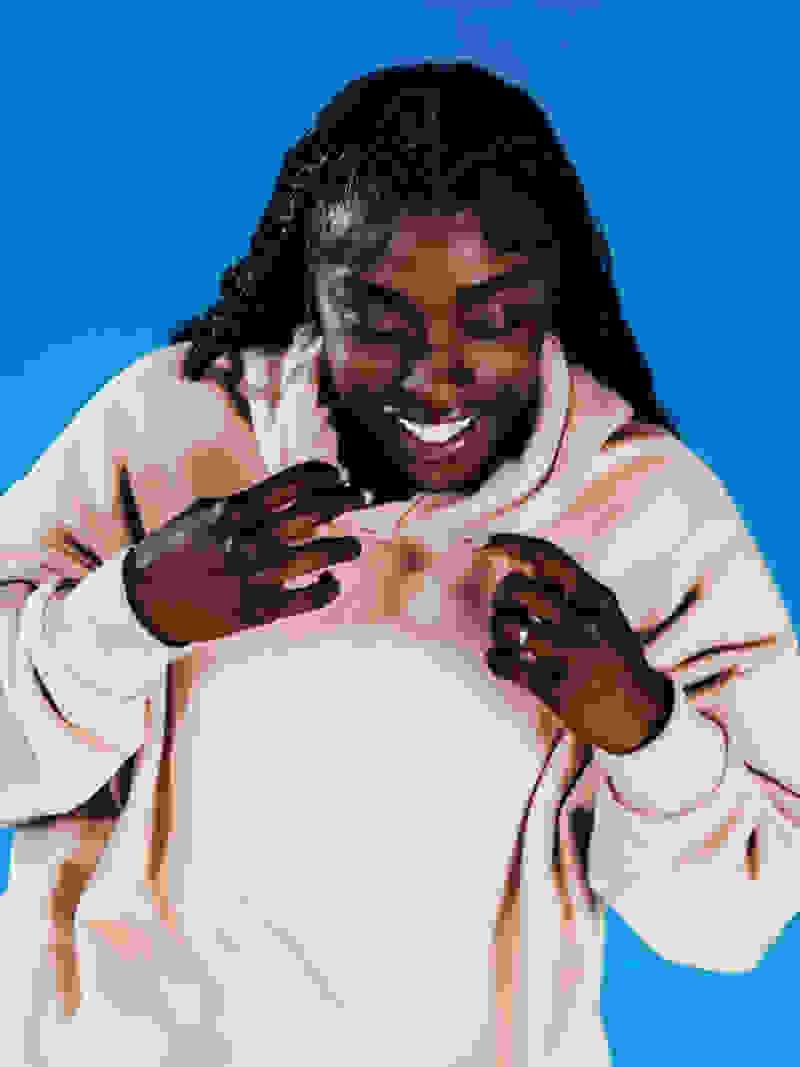 Woman wearing off-white hoodie smiles and looks down in front of blue background
