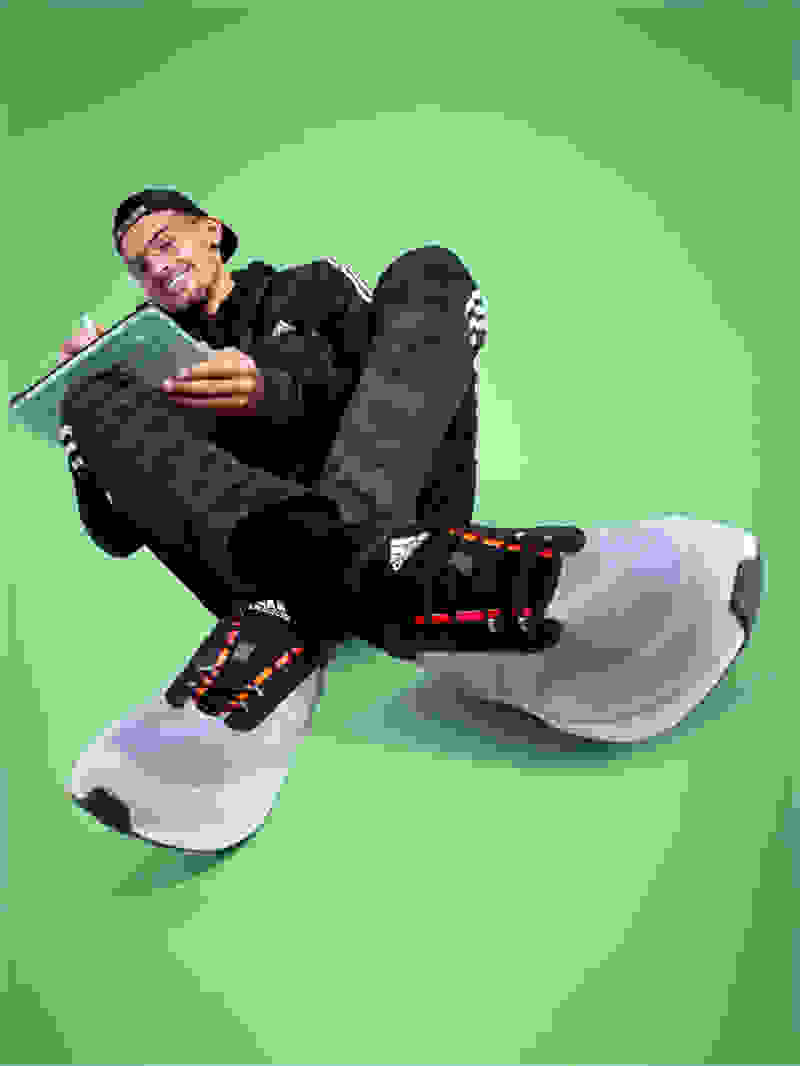Basketball player Trae Young, dressed in black adidas tracksuit and sneakers, shuffles a deck of cards.