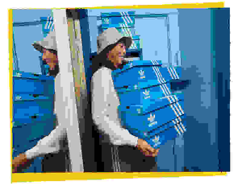 A woman carries 4 boxes of adidas sneakers on the background of a blue door