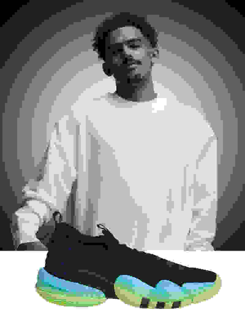 Professional basketball player Trae Young wearing a white long sleeve shirt with a black and teal shoe in the front.