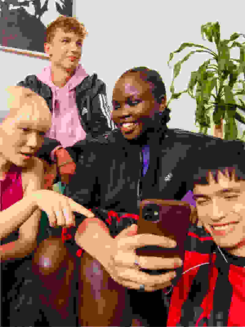 Four smiling individuals posed on a couch together, pointing and looking at a phone screen.