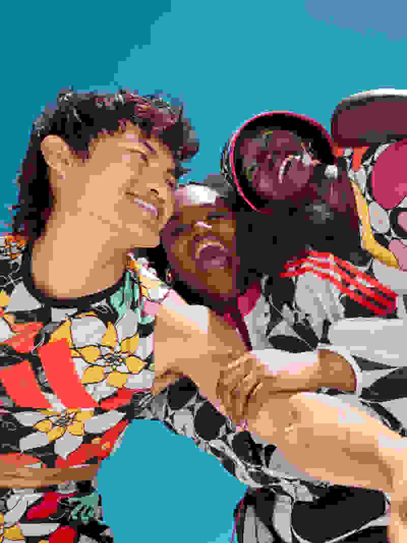 Three adults (1 male and 2 female) are laughing and sharing a joyful moment together. They’re styled in apparel from the adidas x Rich Mnisi Pride Collection.