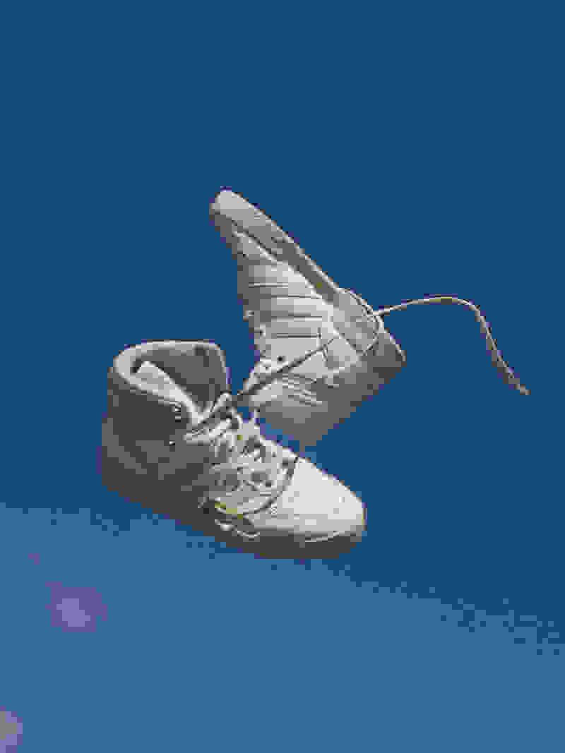 A pair of unlaced white high-top adidas Forum sneakers in front of a blue sky.
