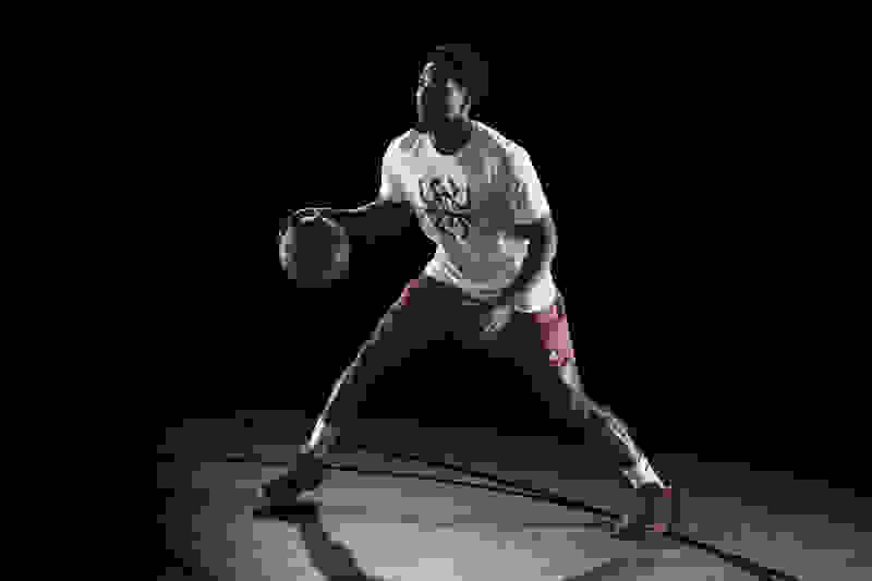 Professional basketball player Donovan Mitchell dribbling on a hardwood court in front of an all-black background.