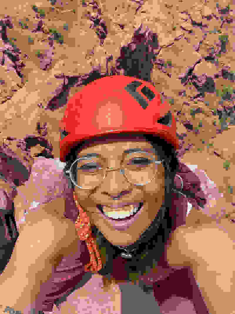 Female climber on a rock face wearing a red helmet smiles at camera
