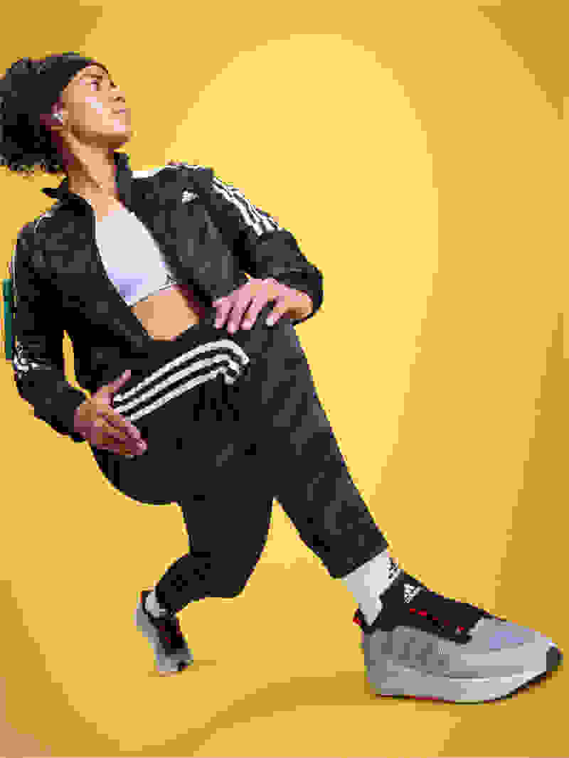 Soccer player Mary Fowler posed mid-lunge, wearing adidas tracksuit and sneakers with earbuds in.