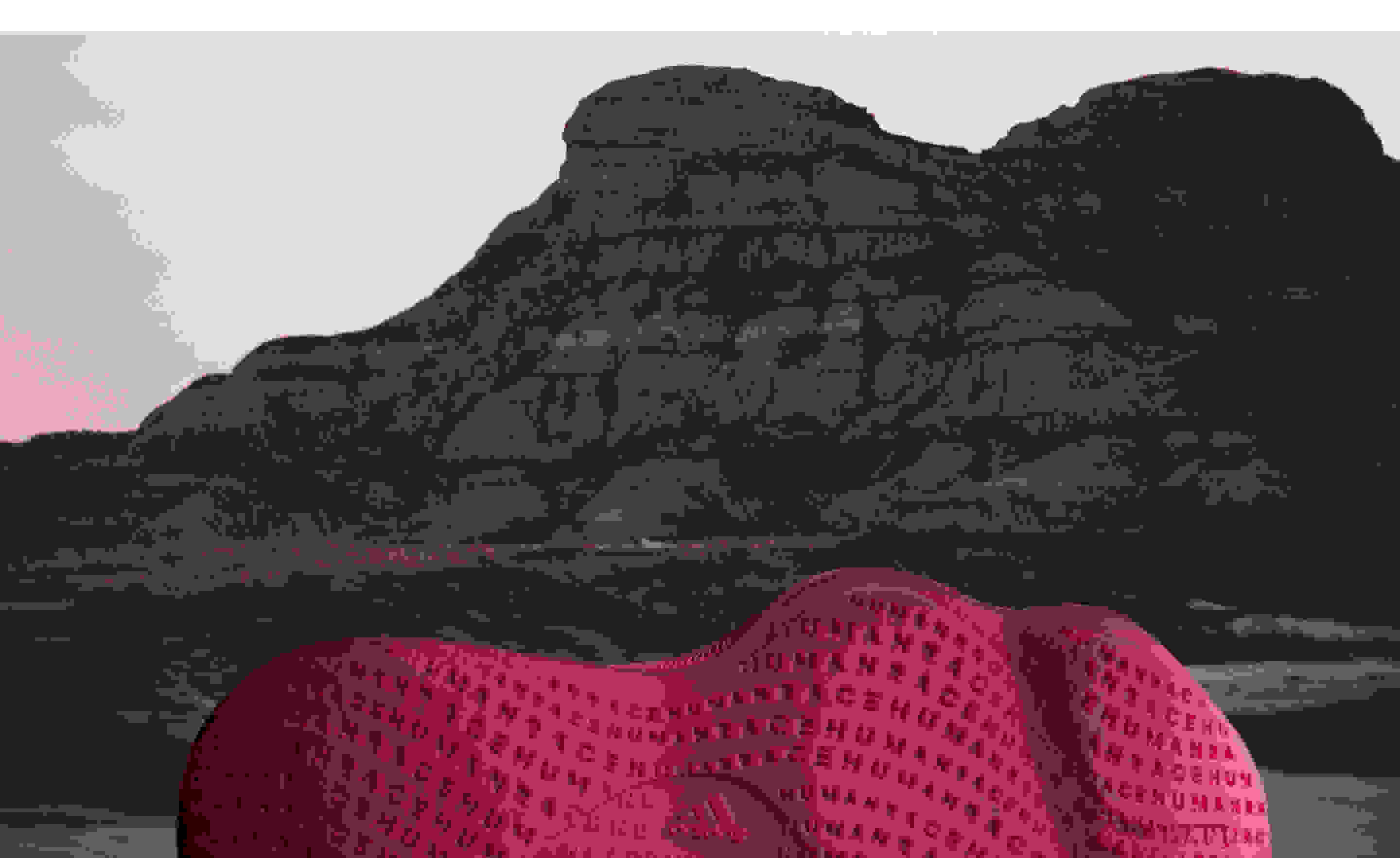 The outsole of a burgundy Humanrace Sičhona shoe against the backdrop of a mountain and tinted sky.