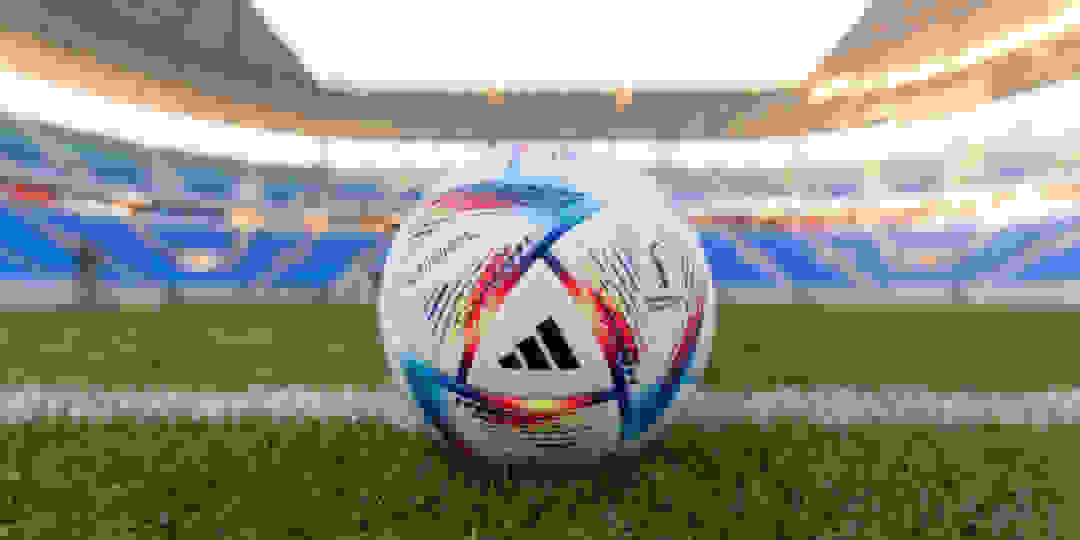 Kolorowa piłka do rugby spoczywa na bujnym, zielonym boisku, otoczonym dużym stadionem z rzędami siedzeń i transparentami.