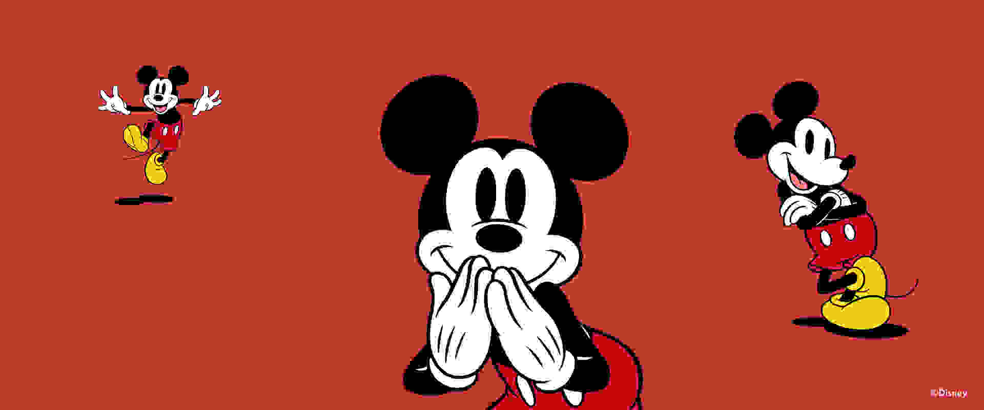 Iconic Disney character Mickey Mouse is prominently featured in the foreground, with his signature black ears and hands covering his face in a playful gesture, set against a vibrant red background.