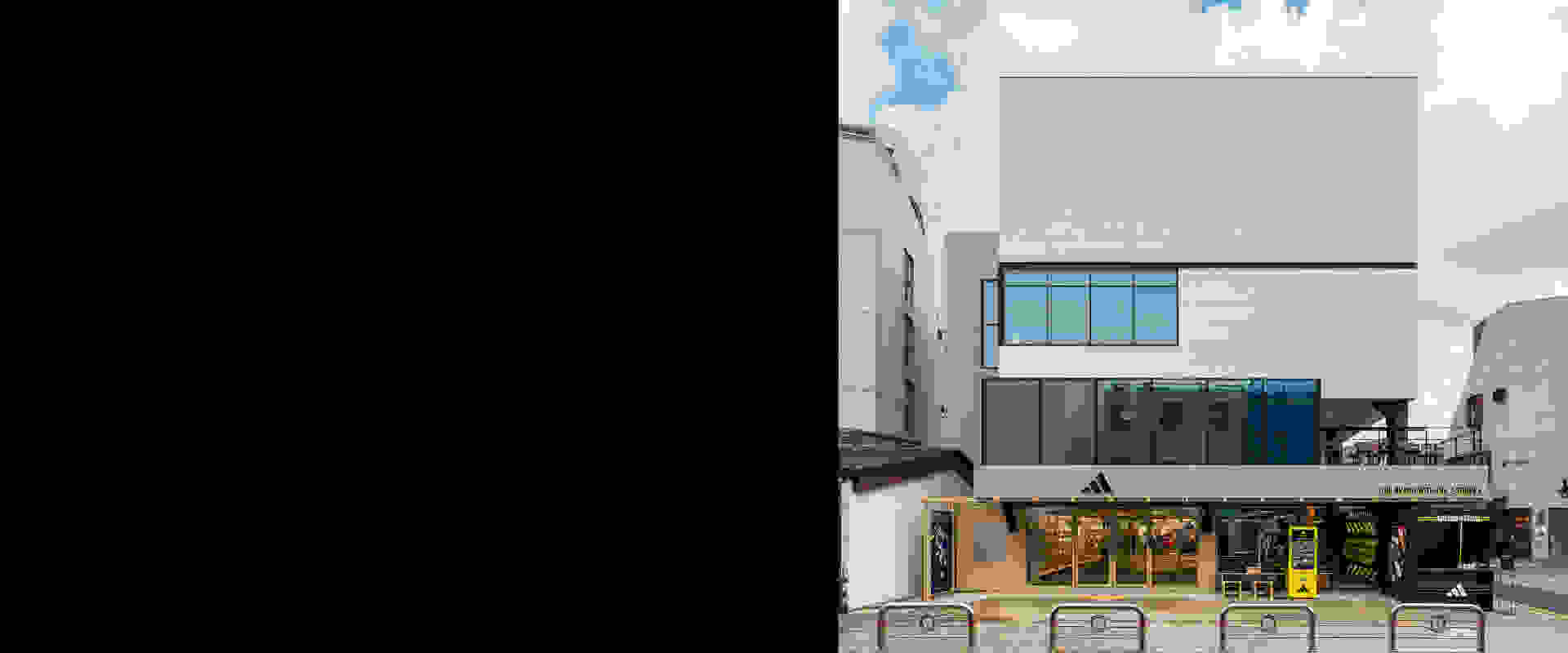 A modern, multi-story building with glass windows and a storefront in the foreground, set against a cloudy sky backdrop.