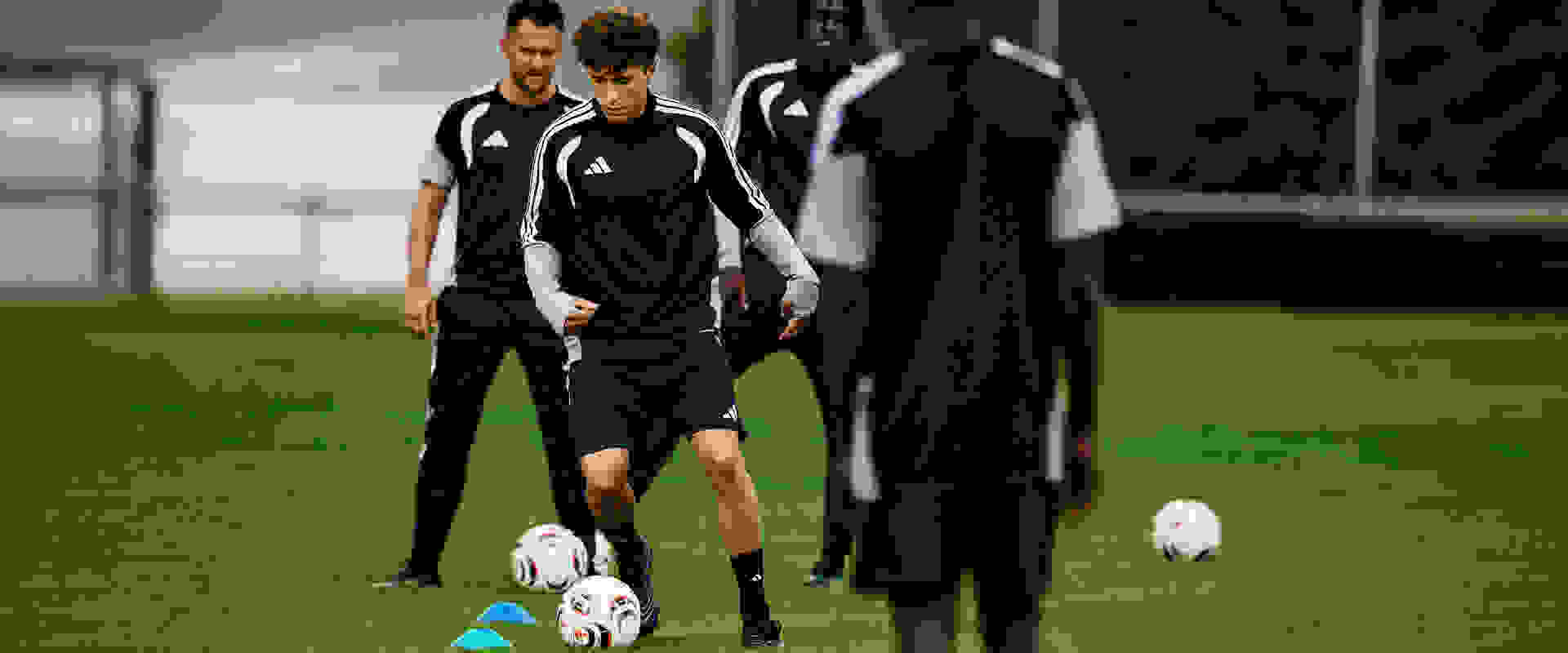 Η εικόνα δείχνει μια ομάδα ποδοσφαιριστών με ασπρόμαυρες εμφανίσεις να περπατάει σε ένα γήπεδο με μπάλα ποδοσφαίρου στο προσκήνιο.