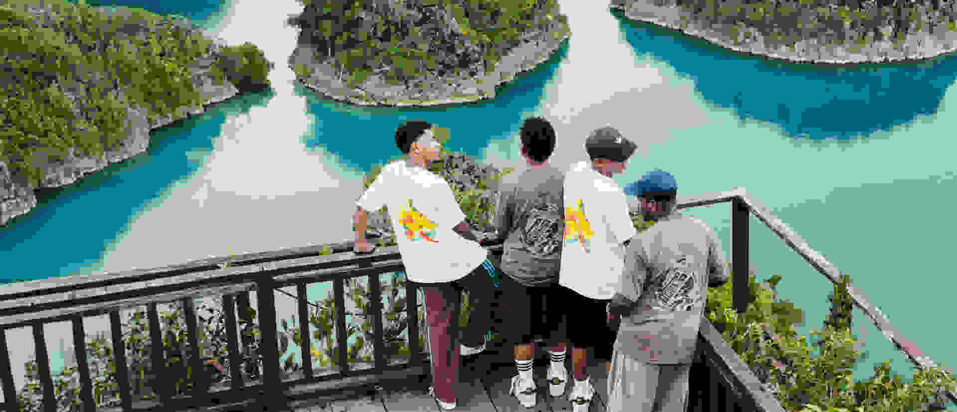 A group of people standing on a wooden platform overlooking a stunning turquoise lagoon surrounded by lush, towering cliffs.
