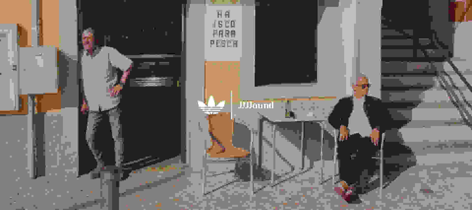 José Mourinho sits outside a café on a cobblestone street wearing the latest adidas Originals x JJJJound collection.