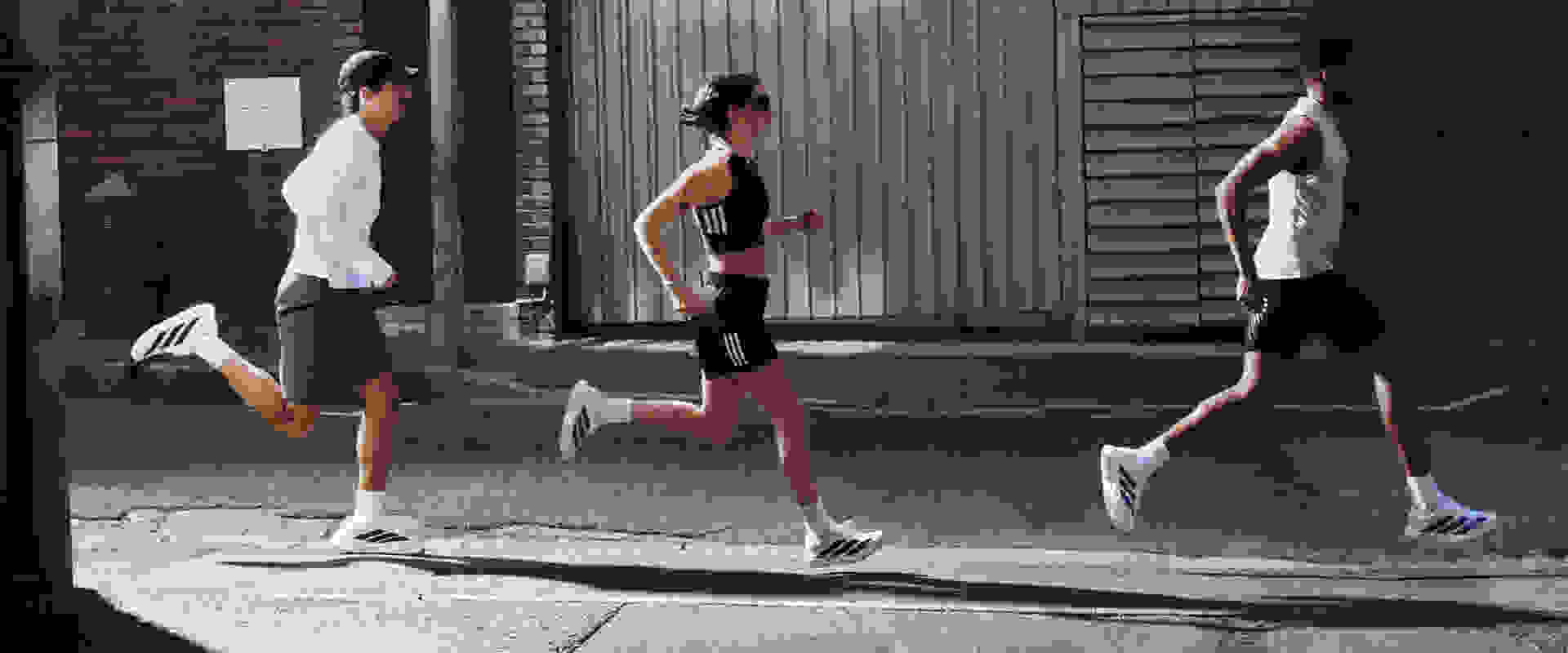 Uma imagem mostrando dois homens e uma mulher correndo com Adizero EVO SLs branco com listras pretas e azuis.