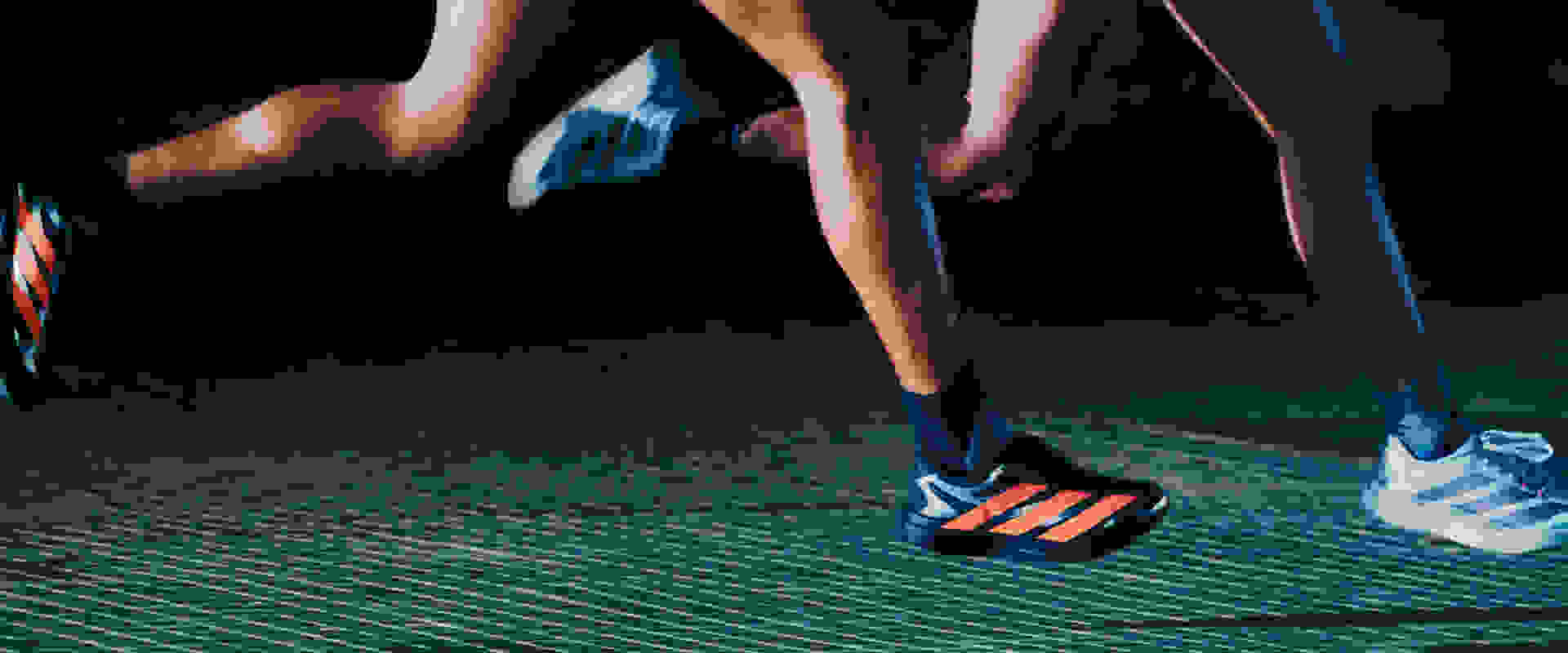 The image shows a close-up view of a person's legs and feet wearing athletic shoes on a dark, textured surface.