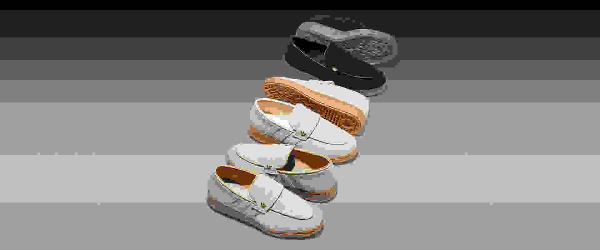 A stack of various casual shoes, including loafers and sneakers, in neutral tones of beige, navy, and yellow, against a plain gray background.