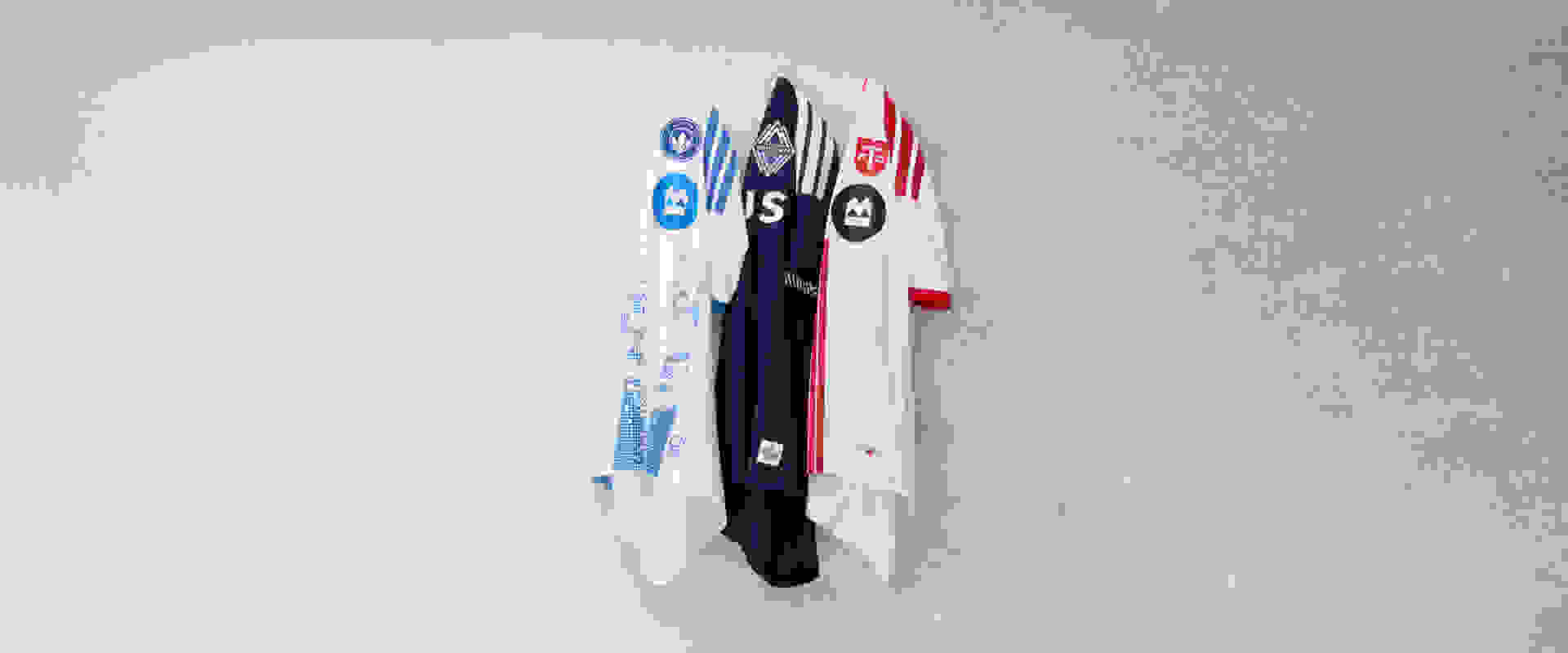 The image shows several white and navy blue shirts or jerseys hanging on a wall, with various logos and designs visible.