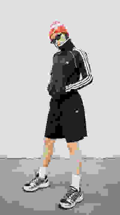 A person wearing a black tracksuit, red hat, and sneakers stands on a plain background.