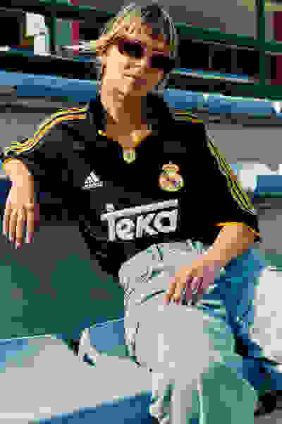A young woman wearing a black and yellow soccer jersey sits on a bench in what appears to be a sports stadium or arena.