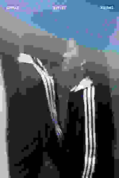 La imagen muestra a una persona con un conjunto adidas de pie frente a un outlet de adidas, con el fondo aparentando ser un entorno urbano borroso.