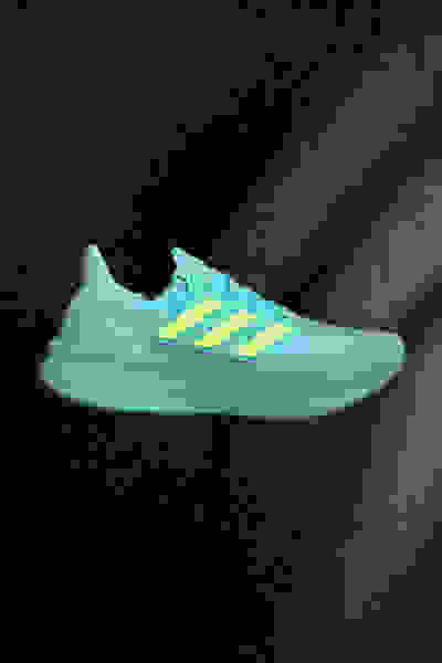 Una vivace scarpa sportiva in giallo e tè è sospesa su uno sfondo scuro e ombreggiato, creando un accattivante contrasto visivo.