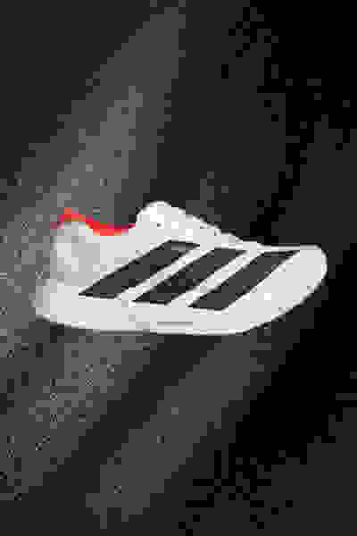 Una scarpa sportiva bianca e nera con dettagli rossi si sviluppa su una superficie scura e testurizzata.