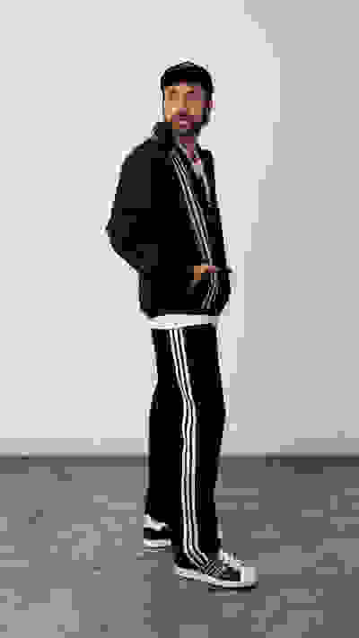 A person wearing a black tracksuit with white stripes, standing in a plain room with a concrete floor.