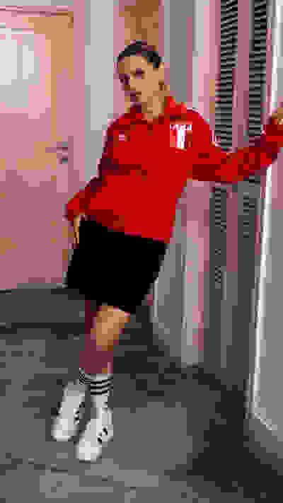 A person wearing a red sports jersey and black shorts stands in a room with a door and window visible in the background.
